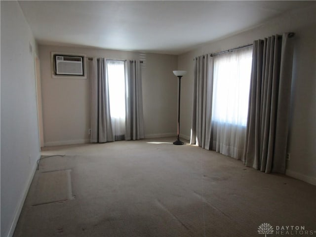 carpeted spare room with a wealth of natural light, a wall mounted air conditioner, and baseboards