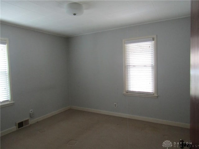 carpeted empty room with a healthy amount of sunlight, visible vents, and baseboards