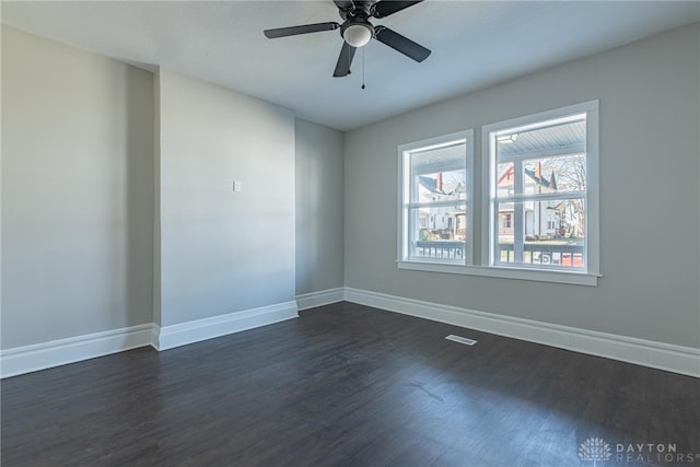 empty room featuring ceiling fan, dark wood finished floors, and baseboards