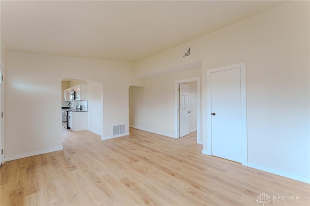 spare room with light wood finished floors, baseboards, visible vents, and arched walkways