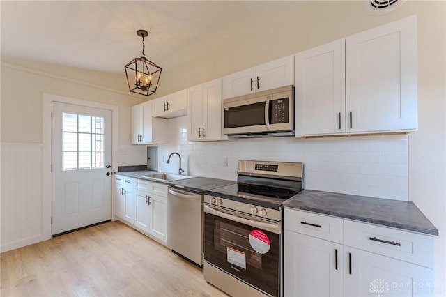 kitchen featuring a sink, light wood-style floors, white cabinets, appliances with stainless steel finishes, and dark countertops