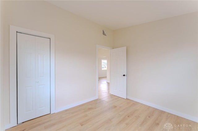 unfurnished bedroom featuring light wood-style floors, baseboards, and a closet