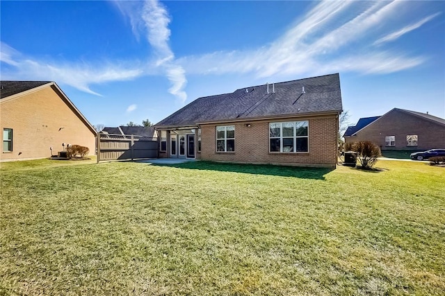 back of house featuring roof with shingles, brick siding, a yard, a patio area, and fence