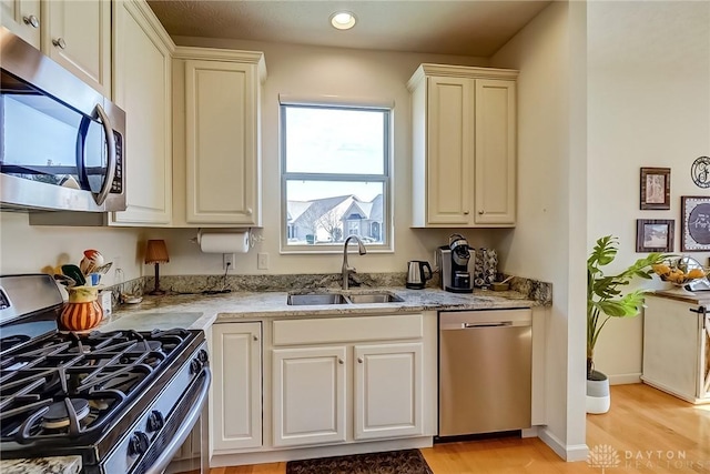 kitchen featuring light wood-style flooring, recessed lighting, stainless steel appliances, a sink, and light stone countertops