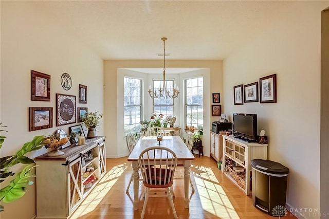 dining space featuring baseboards, light wood-type flooring, and a notable chandelier