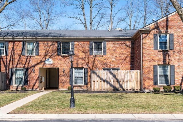 townhome / multi-family property with a shingled roof, brick siding, fence, and a front lawn