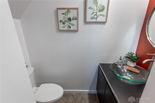 half bathroom featuring toilet, baseboards, wood finished floors, and vanity