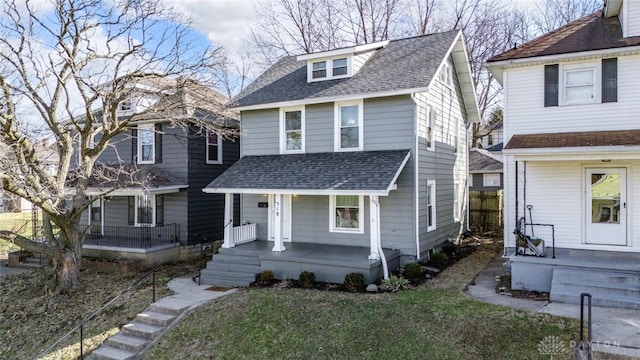 american foursquare style home featuring a front yard, a porch, and roof with shingles