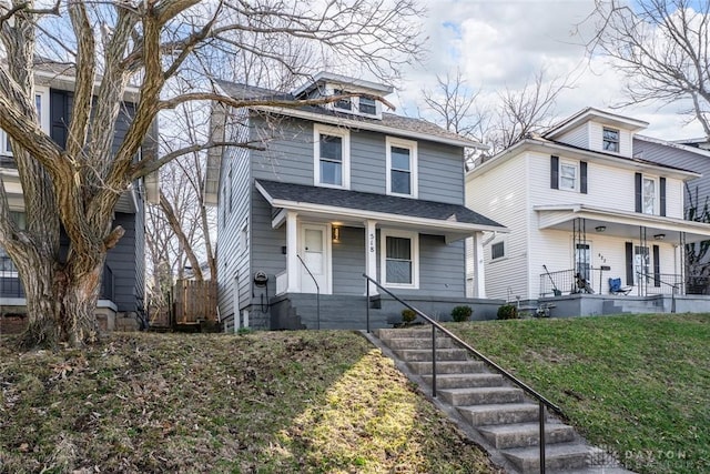 american foursquare style home with a shingled roof, covered porch, and a front lawn