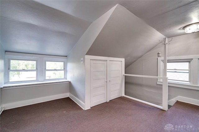 bonus room with vaulted ceiling, dark colored carpet, and baseboards