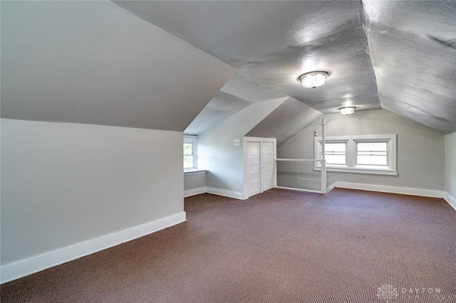 additional living space featuring lofted ceiling, dark colored carpet, a textured ceiling, and baseboards