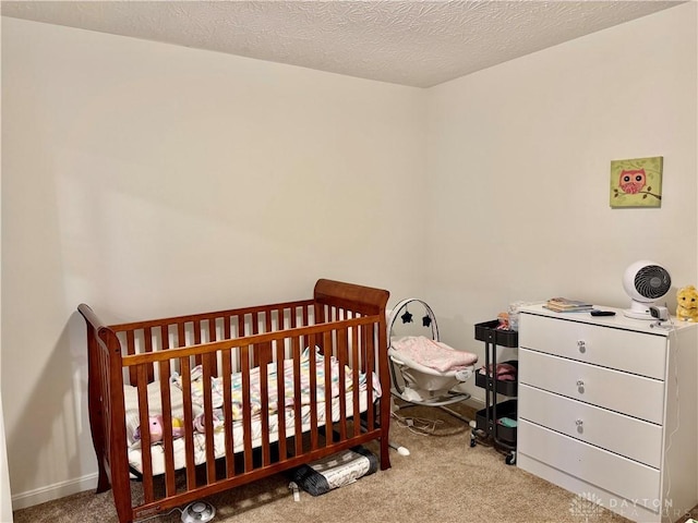 bedroom with carpet floors, baseboards, a textured ceiling, and a crib