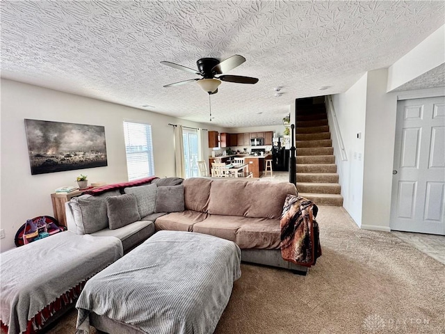 living area featuring a ceiling fan, carpet flooring, a textured ceiling, and stairs