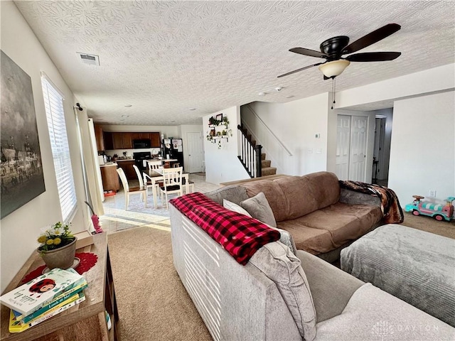 living room with visible vents, light colored carpet, ceiling fan, stairway, and a textured ceiling