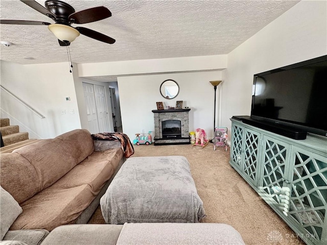 carpeted living area with ceiling fan, a fireplace, stairway, and a textured ceiling