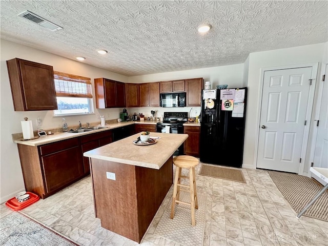 kitchen with visible vents, a kitchen island, light countertops, black appliances, and a sink