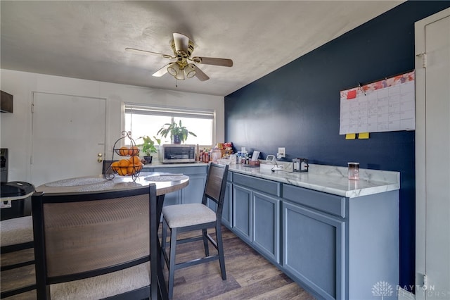 kitchen featuring blue cabinets, wood finished floors, a ceiling fan, light countertops, and stainless steel microwave