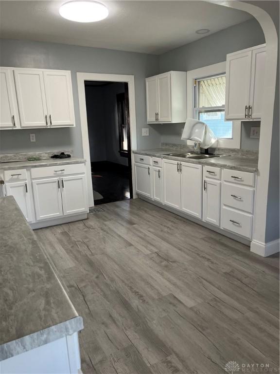 1205 Pursell Ave, Dayton, OH 45420 - kitchen with light wood-type flooring, arched walkways, white cabinets, and a sink