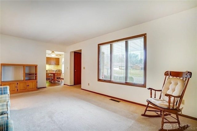 living area with baseboards, visible vents, and light colored carpet