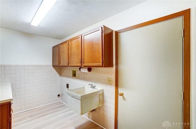 laundry room featuring hookup for a washing machine, a sink, tile walls, light wood-style floors, and cabinet space