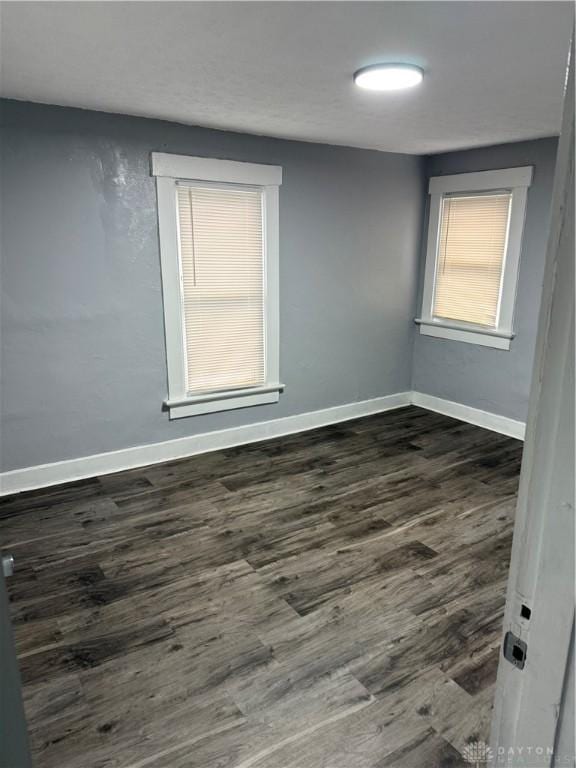 spare room featuring dark wood-style floors and baseboards