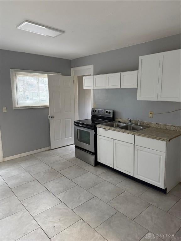 kitchen with light tile patterned floors, baseboards, stainless steel electric range oven, white cabinetry, and a sink