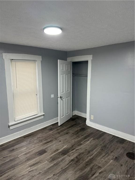 unfurnished bedroom featuring a textured ceiling, dark wood-style flooring, a closet, and baseboards