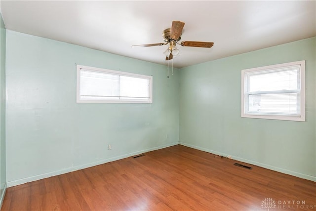 empty room with a ceiling fan, visible vents, baseboards, and wood finished floors