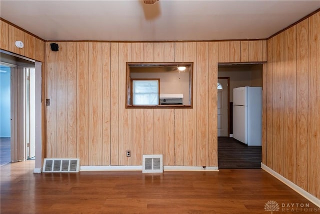 unfurnished room with visible vents, wood walls, baseboards, and wood finished floors