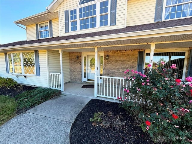 entrance to property with covered porch, brick siding, and a shingled roof