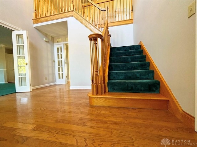 stairway featuring french doors, wood finished floors, a towering ceiling, and baseboards