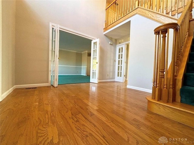 unfurnished room featuring baseboards, a towering ceiling, wood finished floors, stairs, and french doors