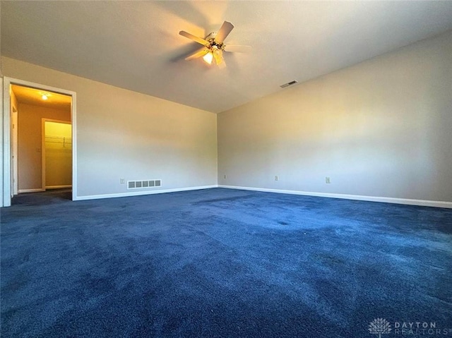 empty room with visible vents, dark carpet, and ceiling fan