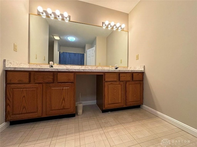 full bathroom with double vanity, a sink, and baseboards