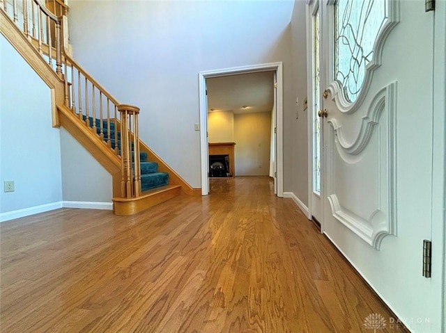 entryway featuring stairs, a fireplace, wood finished floors, and a towering ceiling