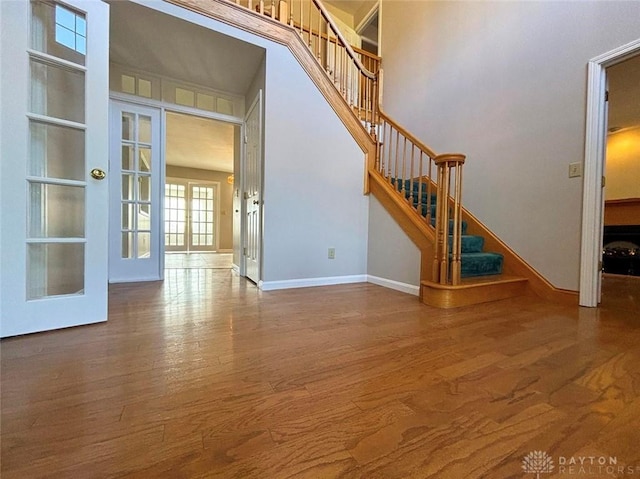 interior space with french doors, stairway, a high ceiling, wood finished floors, and baseboards