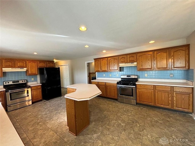 kitchen featuring under cabinet range hood, stainless steel electric stove, stainless steel range with gas stovetop, and freestanding refrigerator