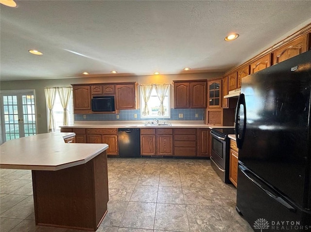 kitchen with under cabinet range hood, light countertops, french doors, decorative backsplash, and black appliances