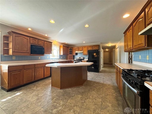 kitchen with under cabinet range hood, a kitchen island, stainless steel range with electric stovetop, freestanding refrigerator, and stainless steel range with gas stovetop