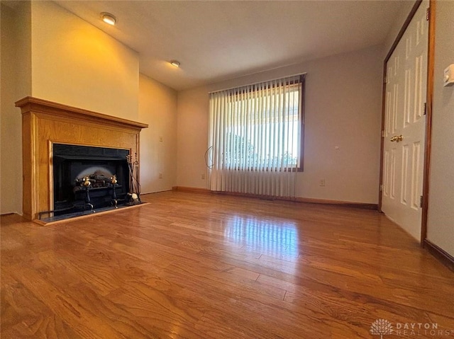 unfurnished living room with lofted ceiling, a fireplace with raised hearth, wood finished floors, and baseboards