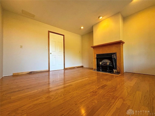 unfurnished living room with lofted ceiling, a fireplace, baseboards, and wood finished floors