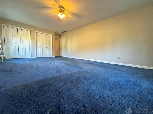 unfurnished bedroom featuring a ceiling fan, baseboards, visible vents, multiple closets, and dark colored carpet