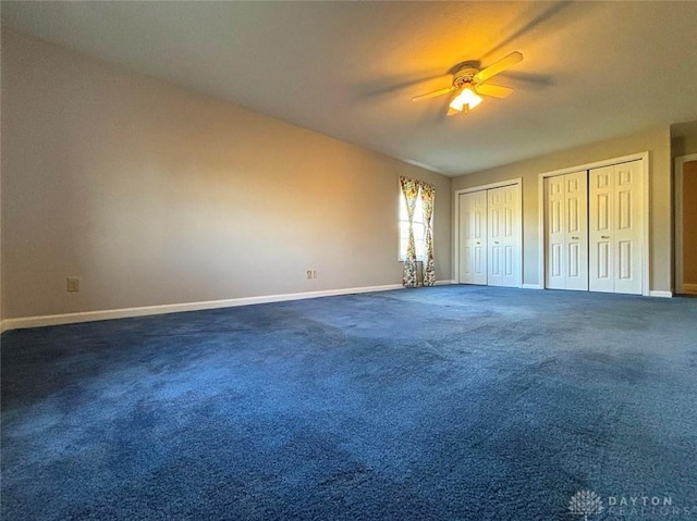 unfurnished bedroom with baseboards, dark colored carpet, a ceiling fan, and multiple closets