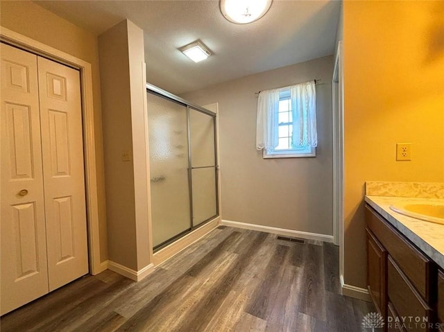 bathroom featuring wood finished floors, a shower stall, vanity, and baseboards