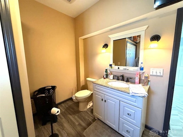 half bath featuring vanity, toilet, wood finished floors, and baseboards