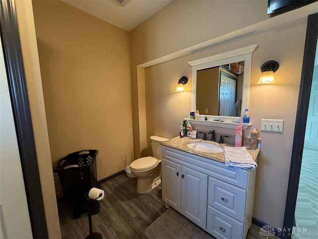 half bath with toilet, vanity, baseboards, and wood finished floors