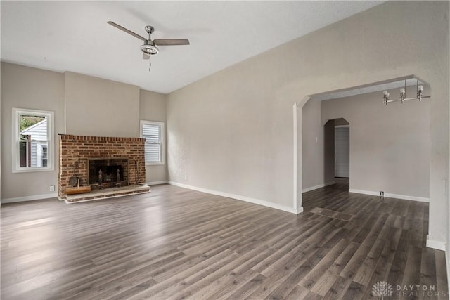 unfurnished living room featuring dark wood-type flooring, a brick fireplace, a healthy amount of sunlight, and ceiling fan