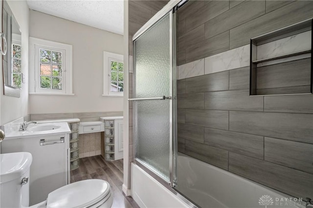 full bath featuring a textured ceiling, toilet, bath / shower combo with glass door, wood finished floors, and vanity