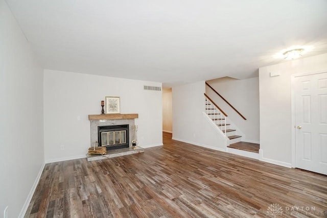 unfurnished living room featuring wood finished floors, visible vents, baseboards, stairs, and a high end fireplace