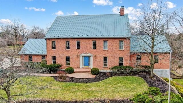 view of front of house featuring metal roof, brick siding, a front yard, a standing seam roof, and a chimney